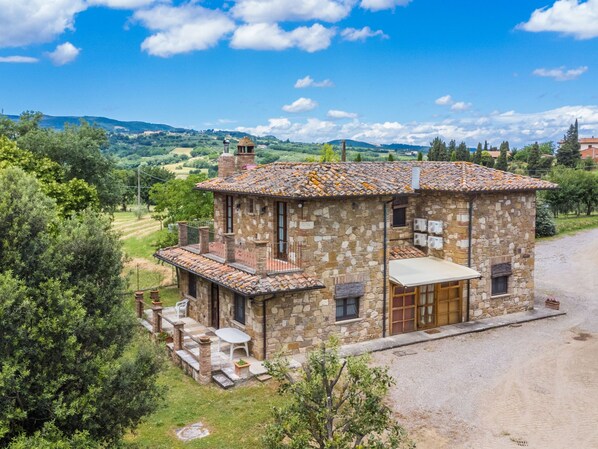 A stone house with a tiled roof, a balcony, and a paved driveway.