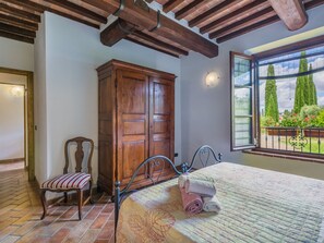 A bedroom with a bed, a wooden wardrobe, a chair, and a window with a view of trees.