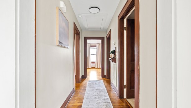 A hallway with wooden floors, a white carpet, and doors on both sides leading to rooms.