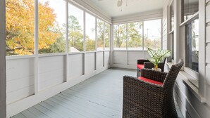A covered porch with a ceiling fan, large windows, wicker furniture, and a potted plant.