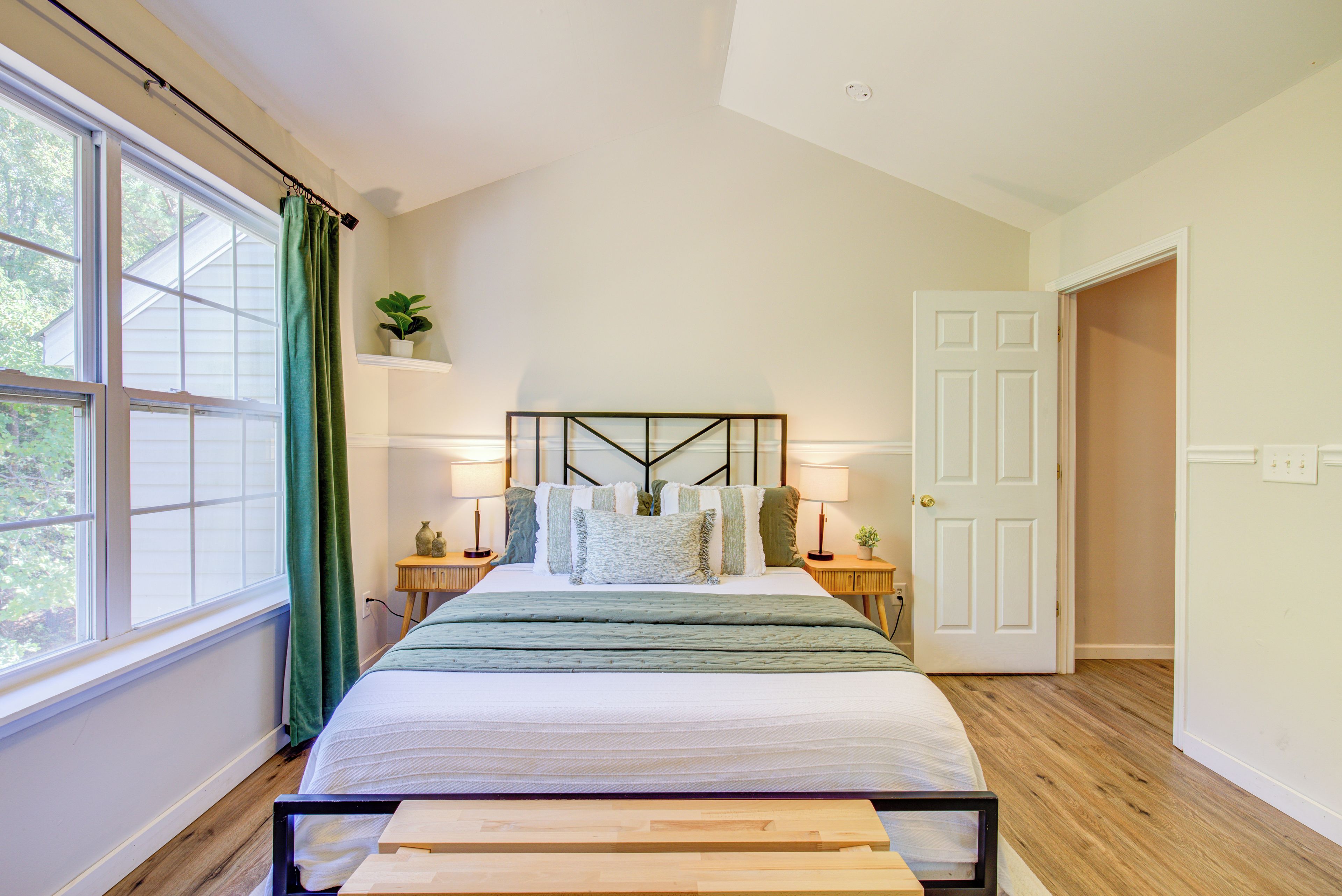 A bedroom with a bed, bedside tables, a window with curtains, and a door.