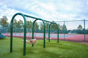 A playground with swings and a tennis court in the background.
