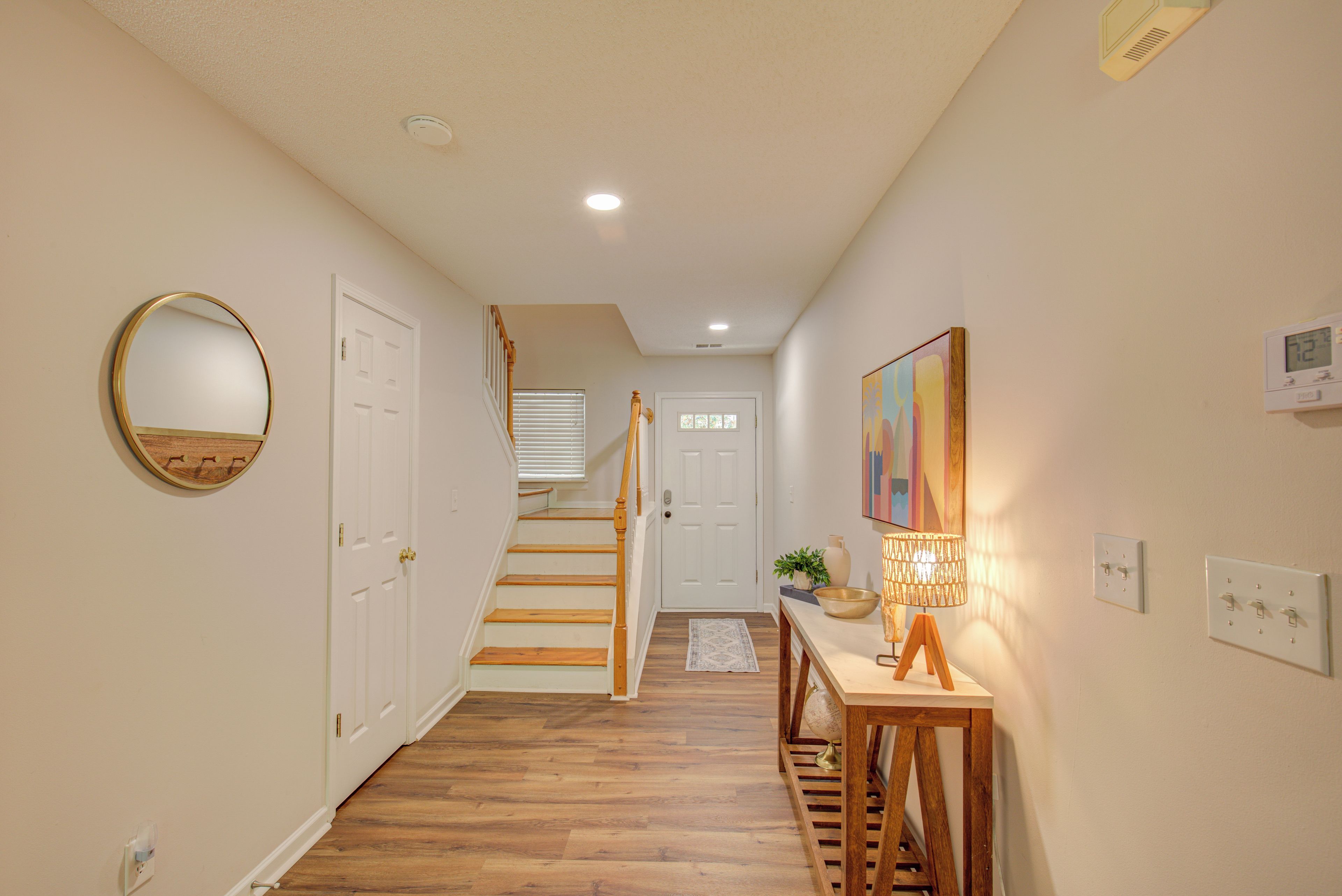 A hallway with wooden flooring, a round mirror, a staircase, and a table with a globe and lamp.