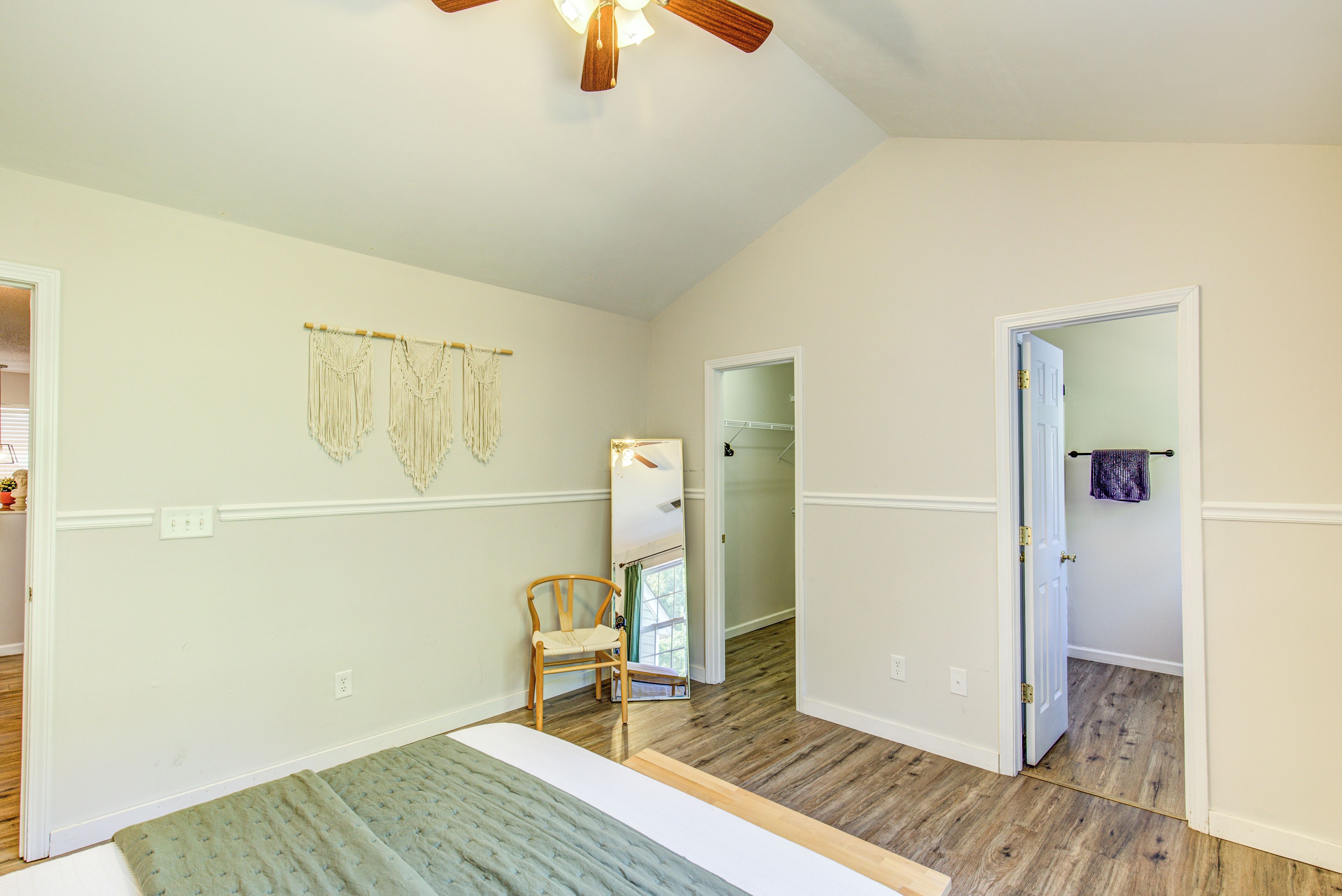 A room with a bed, a chair, a ceiling fan, and a door leading to another room.