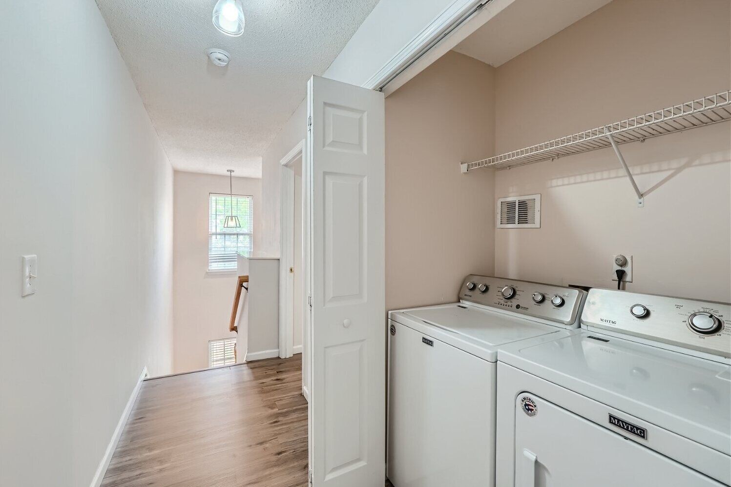 A laundry room with a washing machine and dryer, a window with blinds, and a ceiling vent.