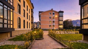 A courtyard with a paved walkway, surrounded by buildings with large windows and a central building with a tower. - Apartamento Rompeolas (Llanes)