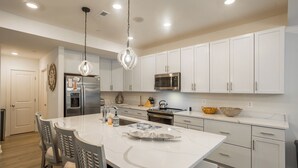 Una cocina moderna con armarios blancos, electrodomésticos de acero inoxidable y una isla central con asientos.