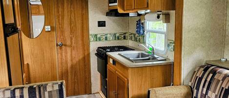 A compact RV interior with a kitchenette, a dining area, and a seating space.