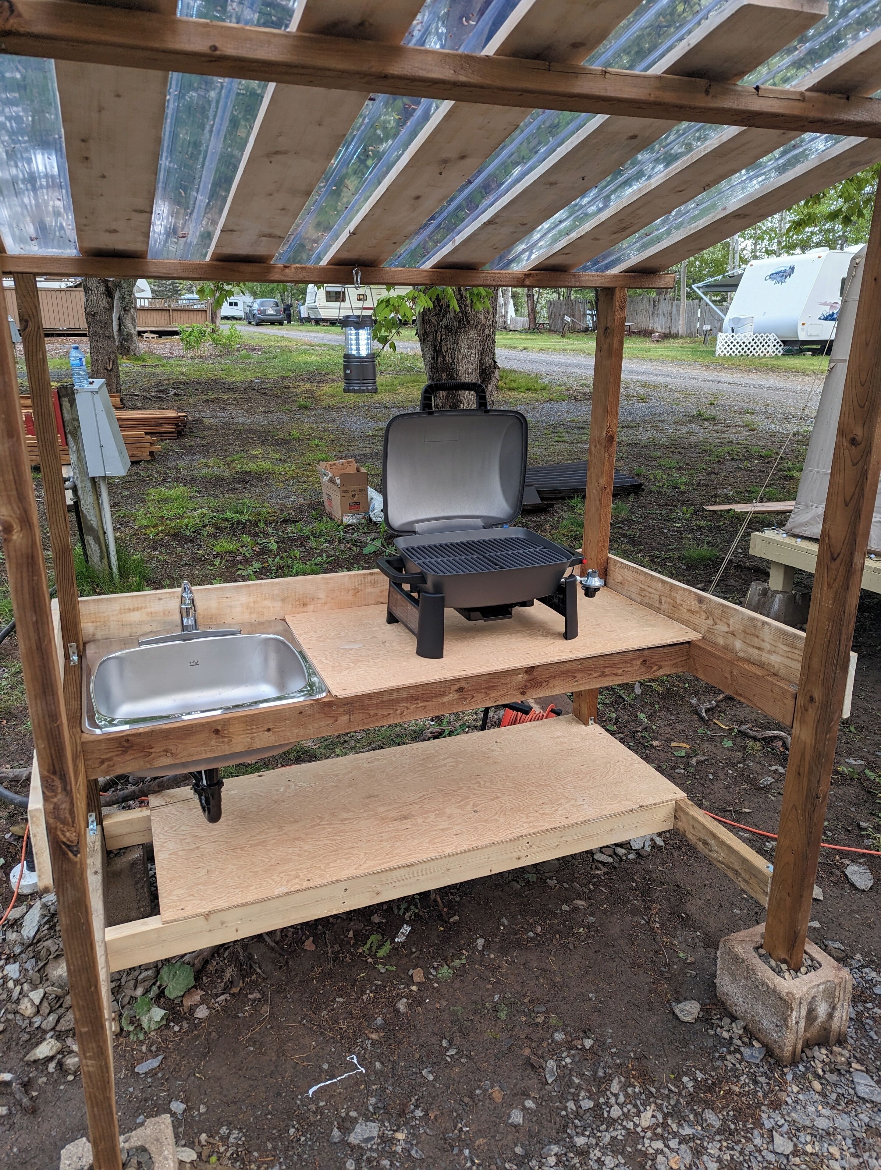A wooden outdoor grill station with a sink and a bench.