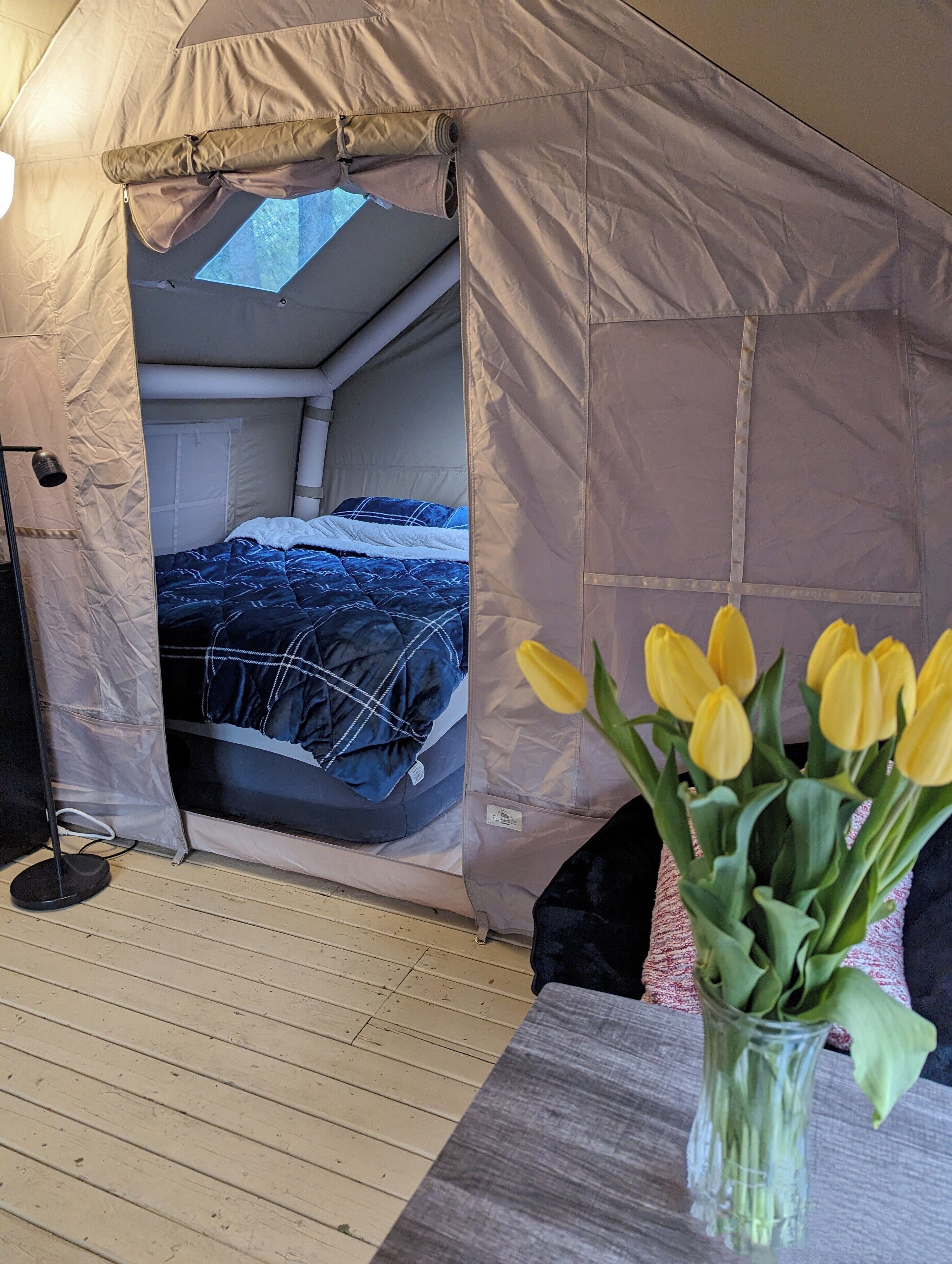 A tent with a bed inside, a small table with a vase of flowers, and a floor lamp.