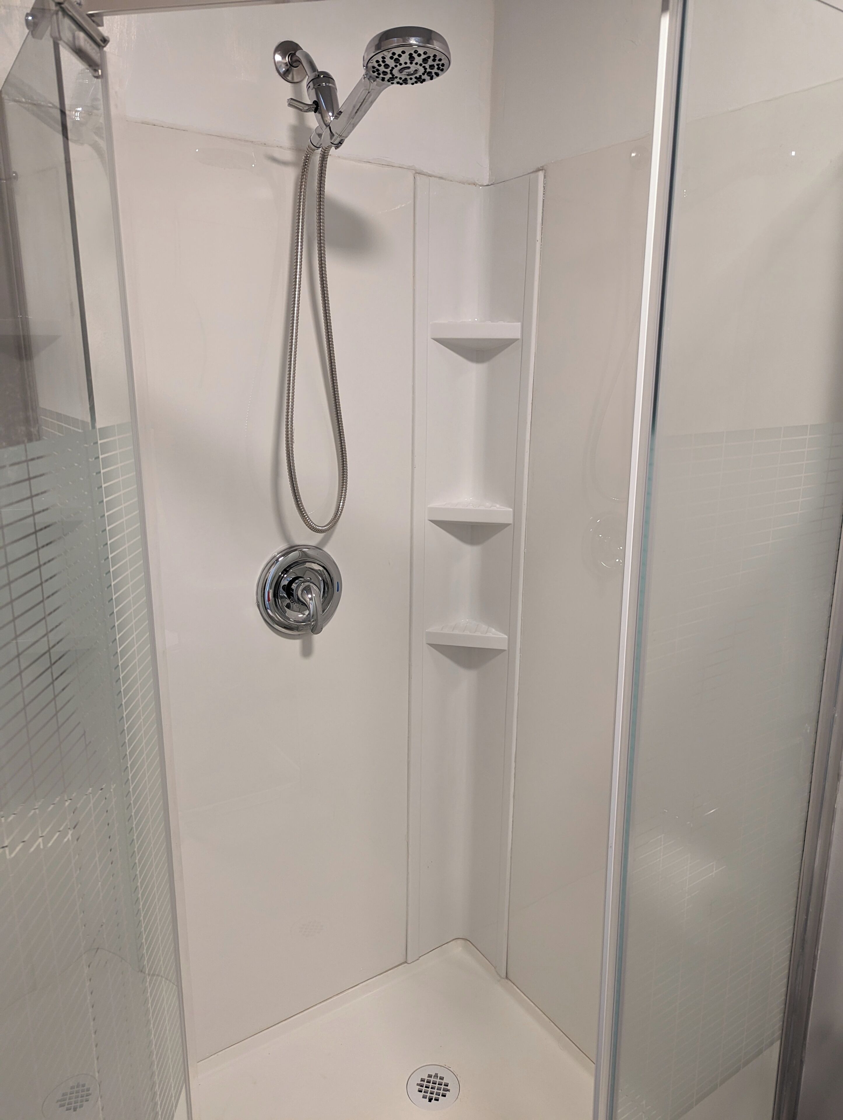Een douche met glazen wand, een handdouche en een kraan op de muur.