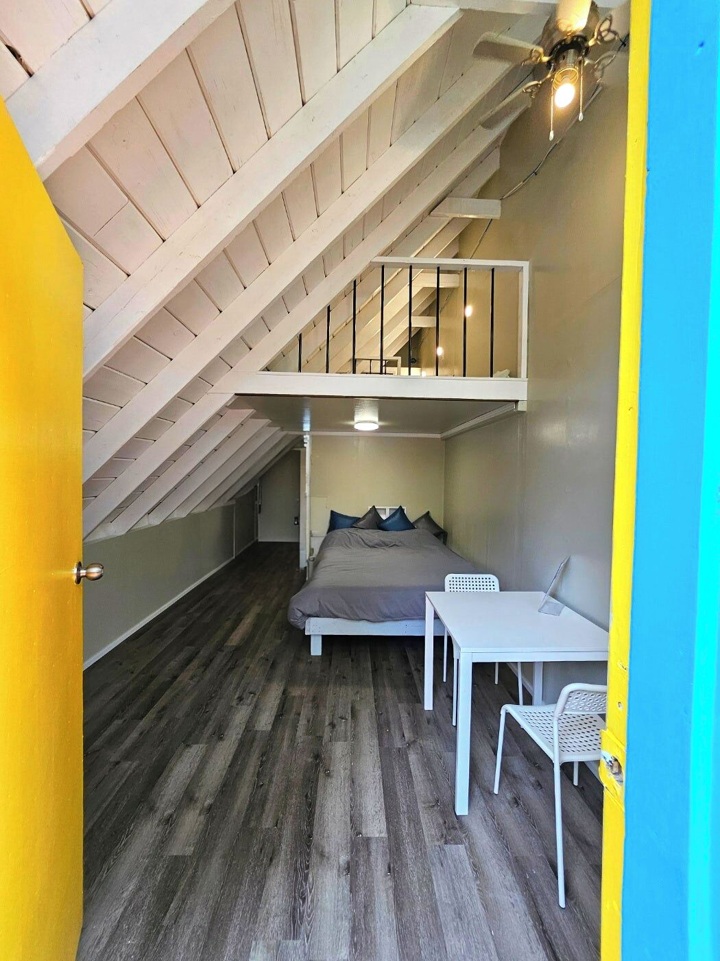 A compact room with a sloped ceiling, a bed, a small table, and a chair.