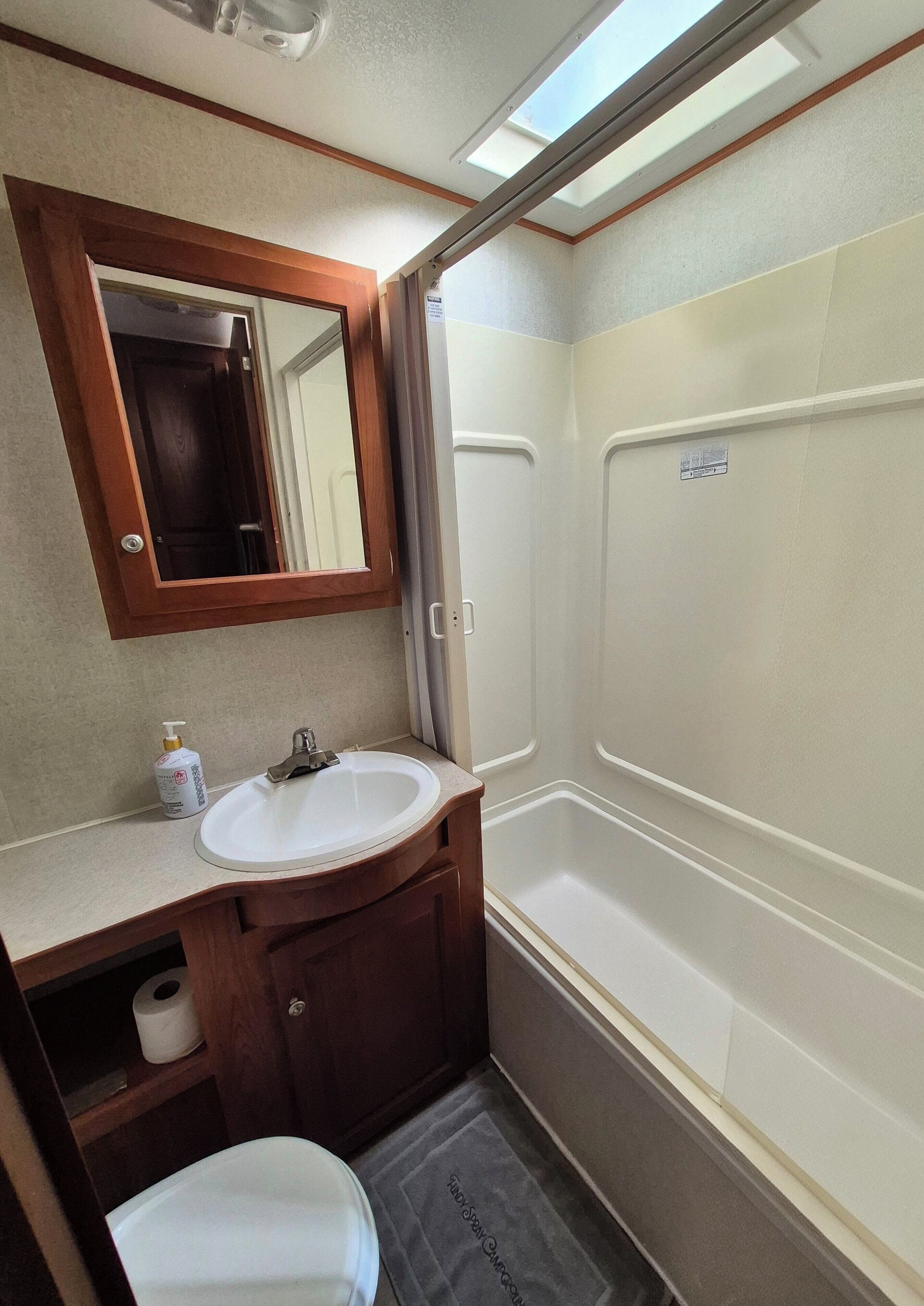 A compact bathroom with a white sink, mirror, and shower.