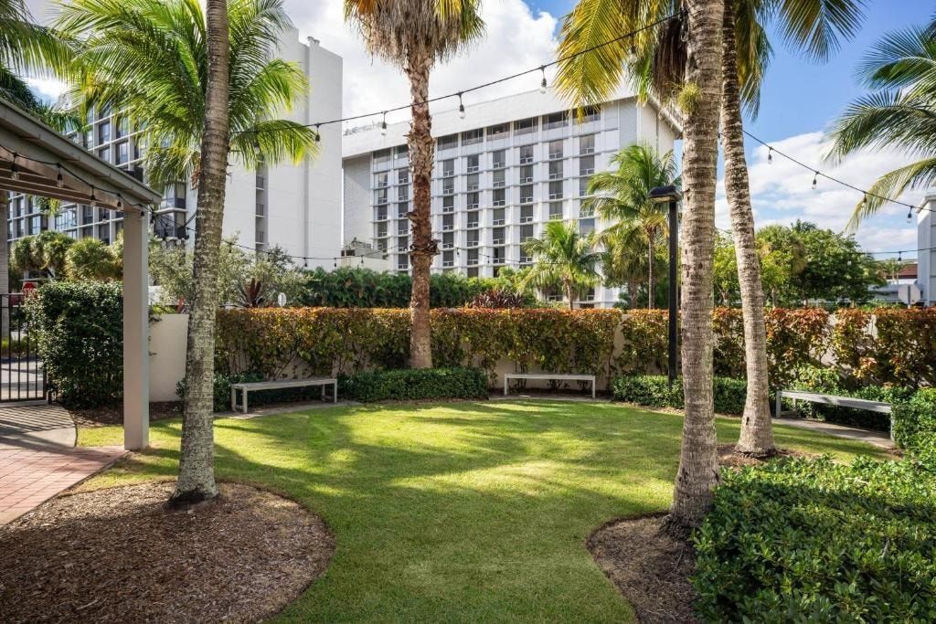 A hotel courtyard with palm trees, a well-maintained lawn, and a building with a modern facade.