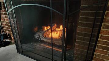 A fireplace with a metal screen, burning logs, and a brick wall in the background.