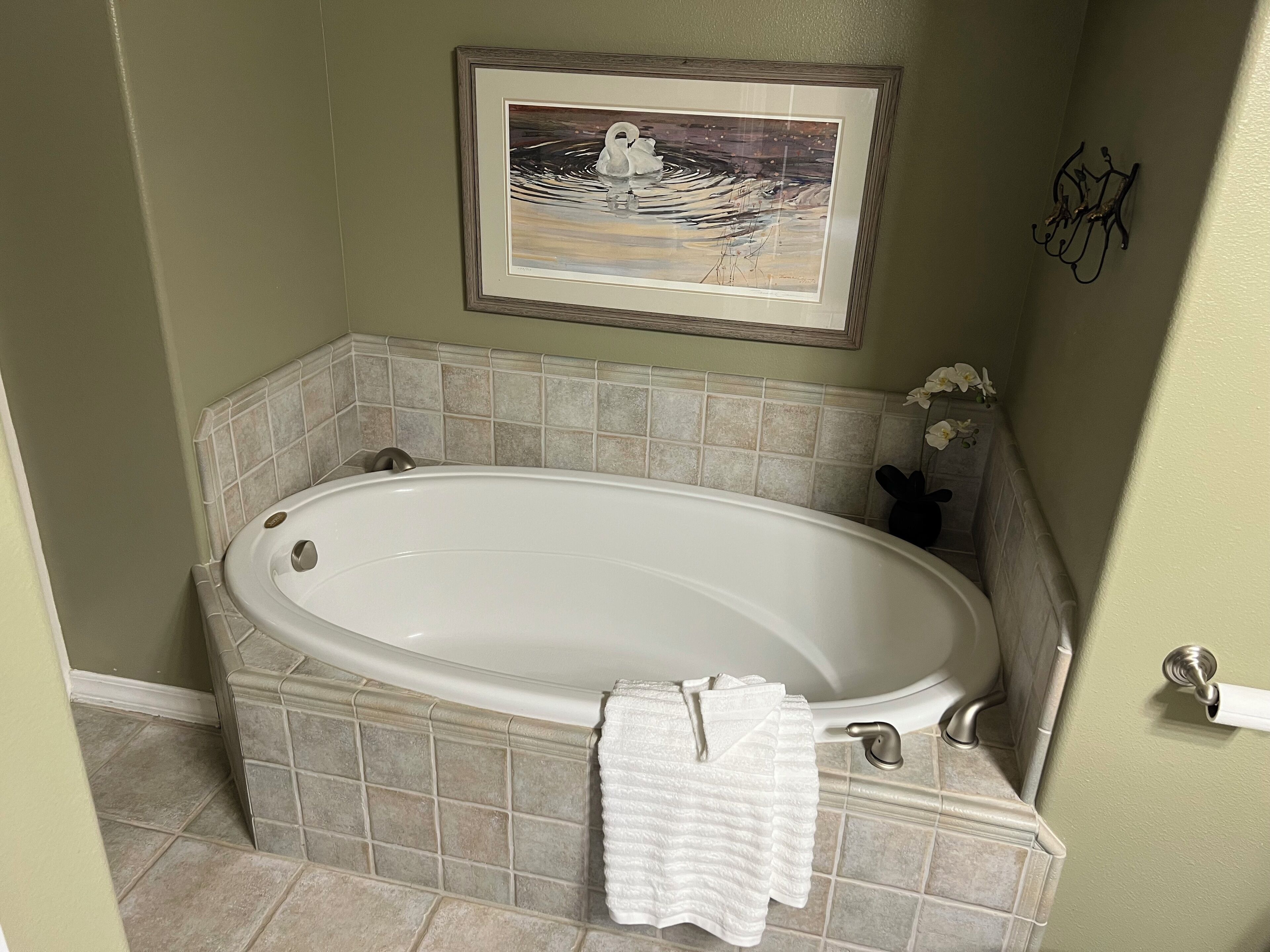 A bathroom with a freestanding bathtub, tiled walls, a framed artwork above the tub, and a small decorative plant.