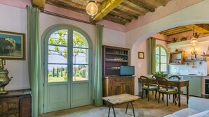 Ein gemütliches Zimmer mit Holzboden, einem Essbereich mit Tisch und Stühlen, einem Fernseher und Blick auf Grünfläche.