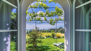 Blick durch ein Fenster auf einen Garten mit Baum, Rasen und einer entfernten Landschaft.