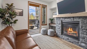 A modern living room with a leather sofa, a fireplace, and a large TV mounted on the wall. - Spring Creek Vacations 1 BR Condo 108TM (Canmore)