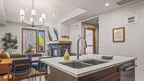 A modern kitchen with a central island, built-in dishwasher, and a dining area with a wooden table and chairs. - Spring Creek Vacations 1 BR Condo 108TM (Canmore)