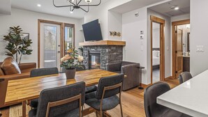 A modern dining area with a wooden table and chairs, a fireplace, and a large mirror on the wall. - Spring Creek Vacations 1 BR Condo 108TM (Canmore)