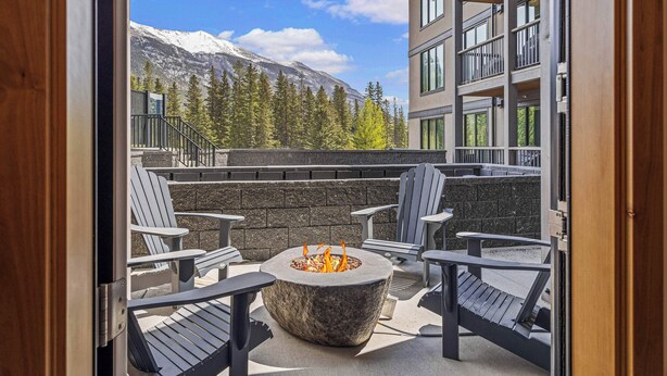 A stone fire pit surrounded by Adirondack chairs, with a mountain view in the background. - Spring Creek Vacations 1 BR Condo 108TM (Canmore)