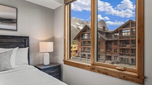 A bedroom with a large window, a bed, a nightstand, and a lamp. - Spring Creek Vacations 2 BR Premier Condo 315TM (Canmore)