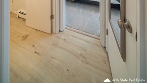 A hallway leading to a bedroom with a bed, a door, and a small bathroom with a towel hanging on the wall. - Your Nordic Retreat (Anchorage)