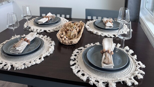 Una mesa de comedor dispuesta con platos, vasos y una cesta decorativa en el centro.