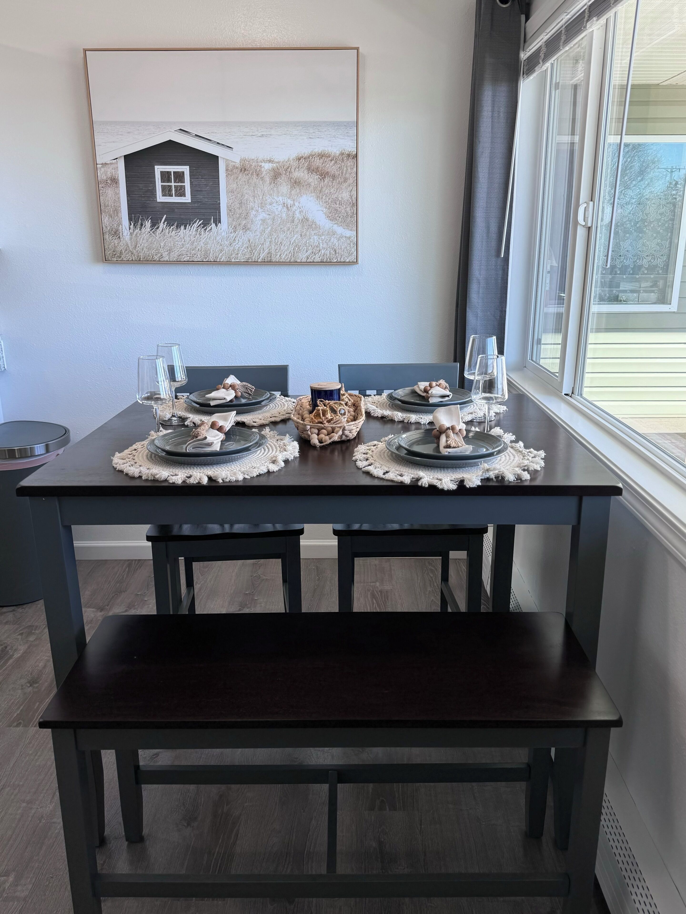 Une table à manger dressée avec des assiettes, des verres et un centre de table, et un tableau accroché au-dessus.