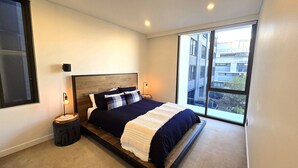 Un dormitorio moderno con una cama grande, dos mesitas de noche y una ventana con vistas a edificios.