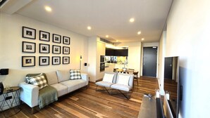 Una sala de estar moderna con un sofá, sillones y una zona de comedor. Hay cuadros en la pared y un televisor a la derecha.