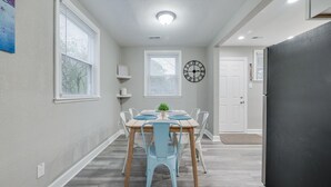 Een eetgedeelte met een houten tafel, blauwe stoelen, een klok en een deur op de achtergrond.