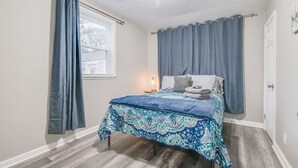 Een slaapkamer met een bed, gordijnen, een bedlamp en een raam.