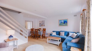 Un salon moderne avec un canapé bleu, une table à manger avec des chaises, un escalier et un tableau accroché au mur.