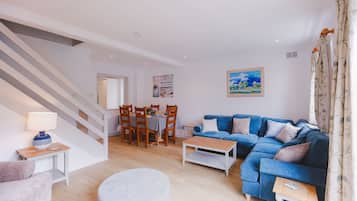 Ein modernes Wohnzimmer mit einem blauen Sofa, einem Esstisch mit Stühlen, einer Treppe und einem Bild an der Wand.