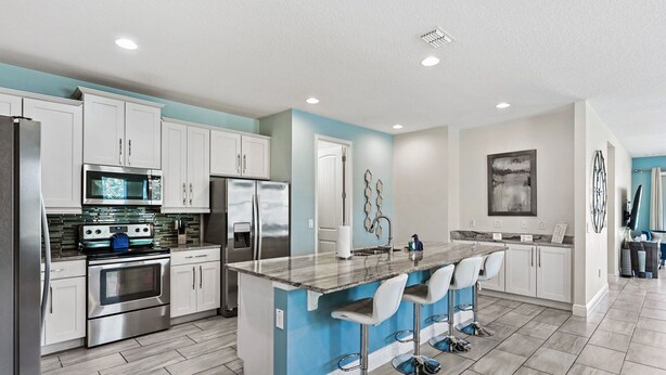 A modern kitchen with white cabinets, stainless steel appliances, a blue accent wall, and a central island with bar stools. - 8BR Modern Family Villa • Game Room • Near Disney (Kissimmee)
