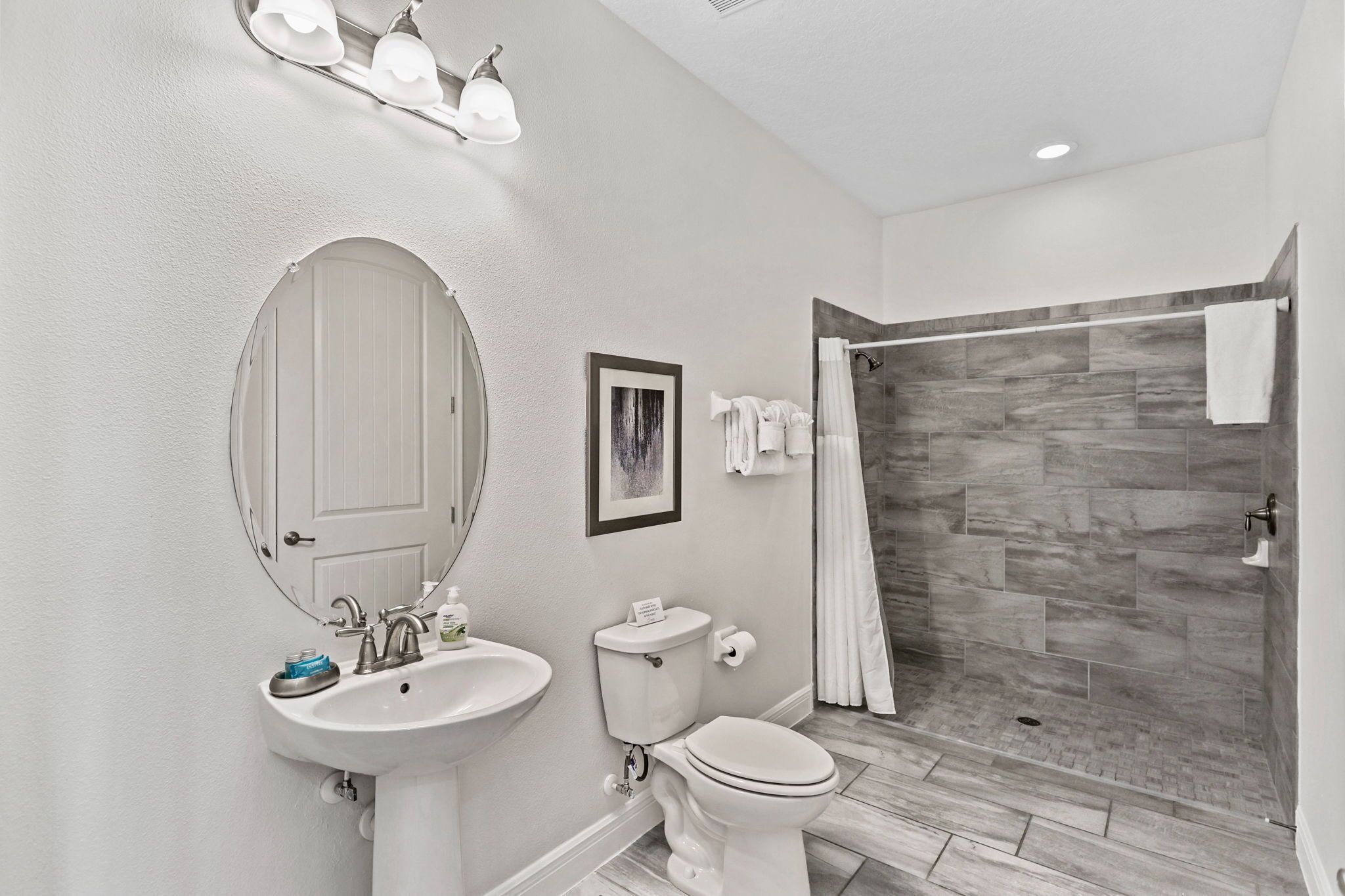 A modern bathroom with a white sink, toilet, and shower area with grey tiles.