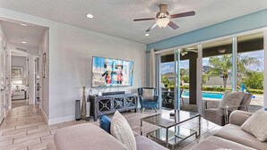 A spacious living room with a large flat-screen TV, comfortable seating, a glass coffee table, and a ceiling fan. - 8BR Modern Family Villa • Game Room • Near Disney (Kissimmee)