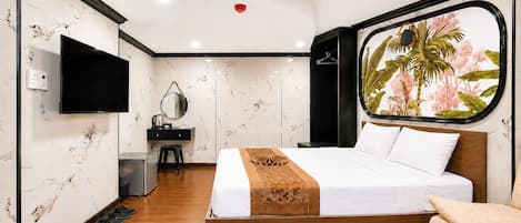 Hotelkamer met een bed, bureau, stoel, televisie en raam met uitzicht op palmbomen.