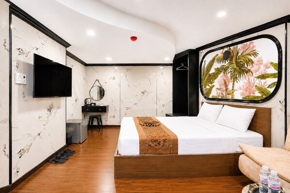 A hotel room with a bed, a desk, a chair, a TV, and a window with a view of palm trees. - Red Sun Airport Saigon Hotel (Ho Chi Minh City)
