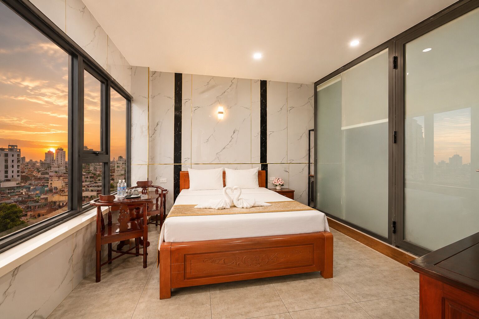 Une chambre d’hôtel moderne avec un grand lit, un bureau et une chaise. La fenêtre offre une vue sur la ville.