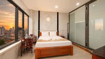 A modern hotel room with a large bed, a desk, and a chair. There is a city view through the window.