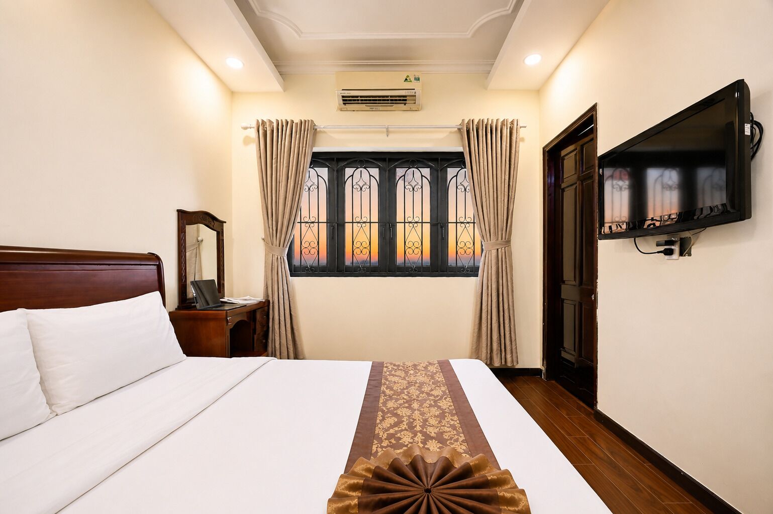 Habitación de hotel con cama, escritorio con computadora portátil, televisor montado en la pared y ventana con cortinas.