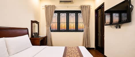 Une chambre d’hôtel avec un lit, un bureau avec un ordinateur portable, un téléviseur fixé au mur et une fenêtre avec des rideaux.