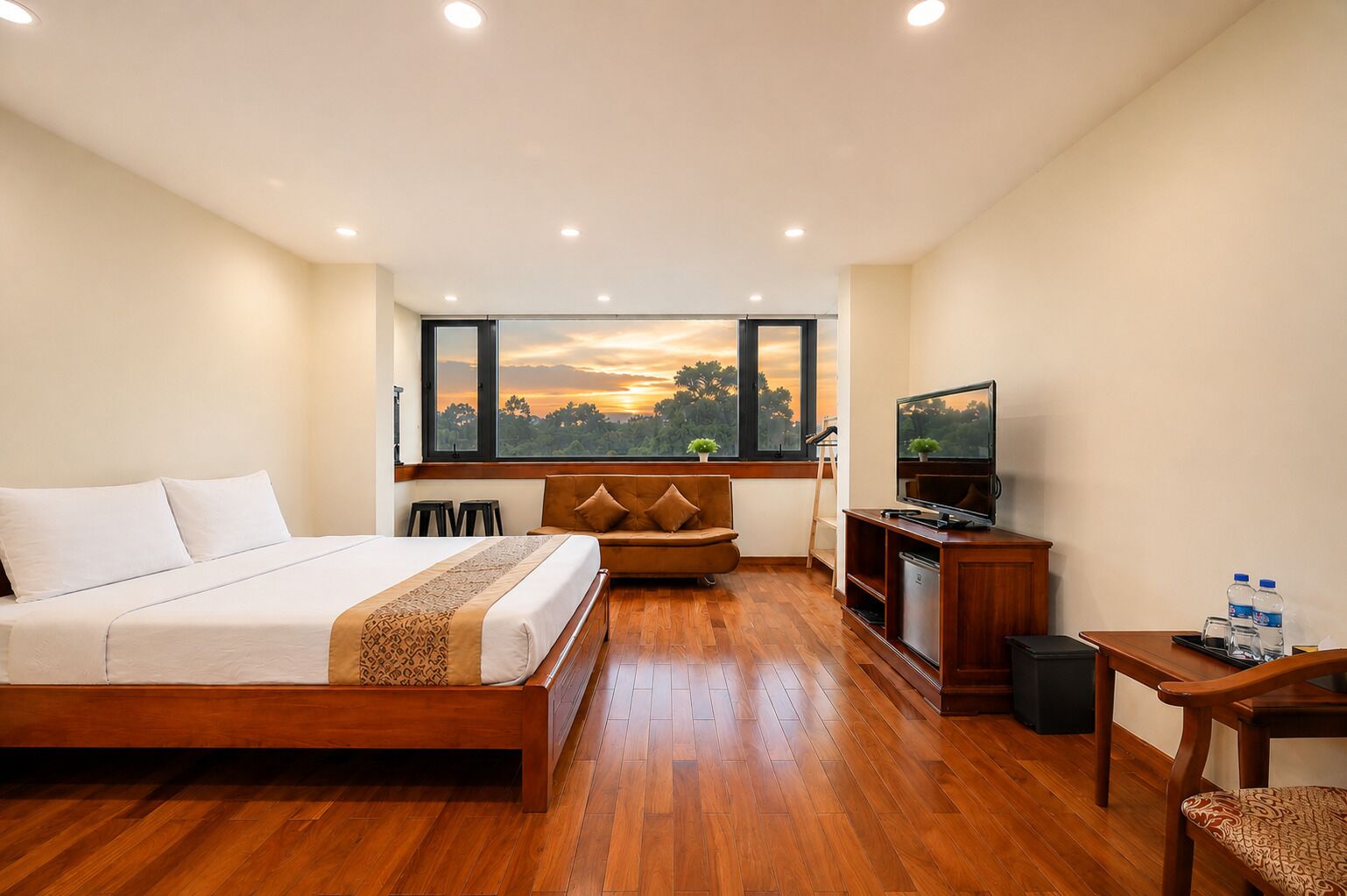 Habitación de hotel con cama, sofá, televisor y escritorio con botellas de agua.