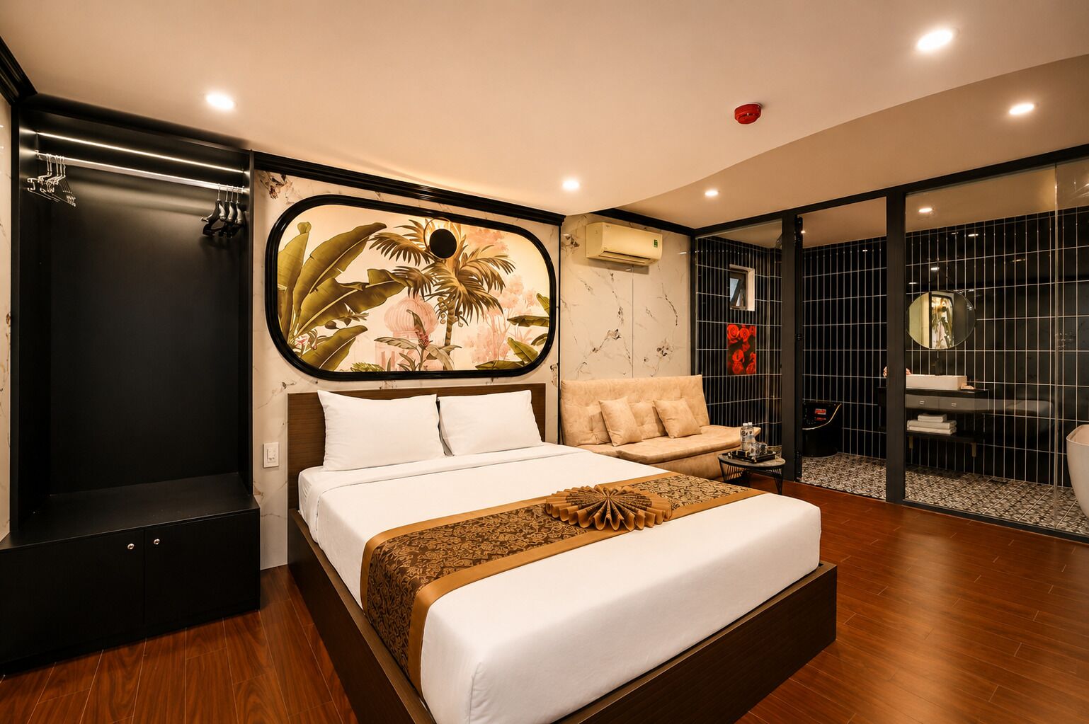 A modern hotel room with a large bed, a sofa, a small table, and a bathroom with a mirror and sink.
