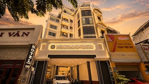 The Red Sun Airport Hotel entrance with a white car parked in front, surrounded by trees and other buildings.