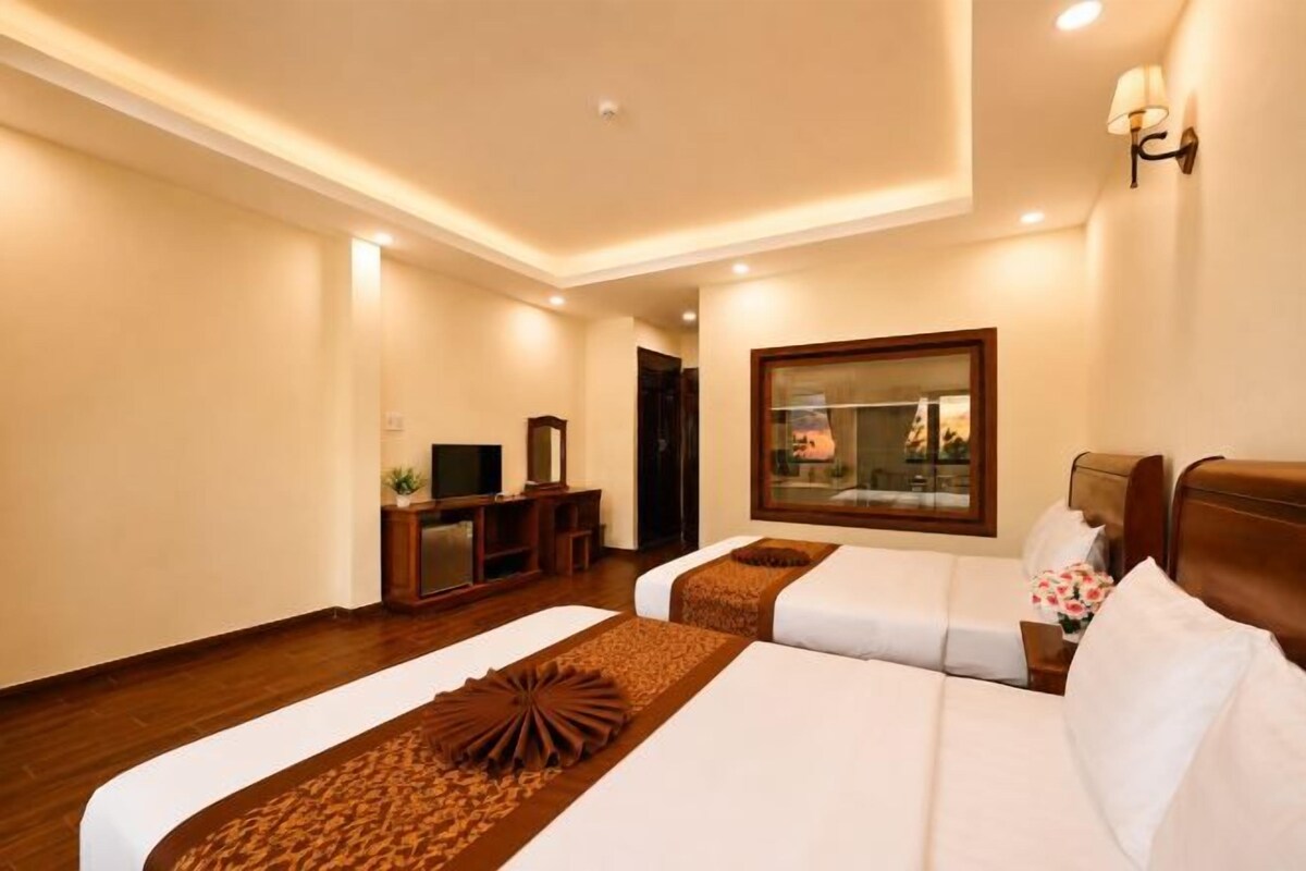 A hotel room with two beds, a desk, a TV, and a large window.