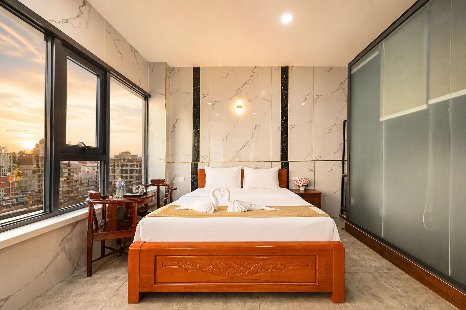 A hotel room with a large bed, a desk, and a chair, a window with a city view, and marble walls.